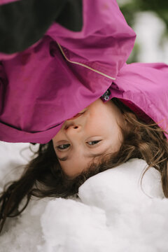 Child in pink jacket lying playfully upside down in snow