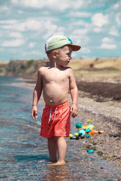 Little boy standing in the sea, toys in the background
