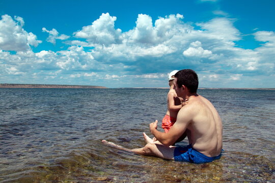 A baby and his father sit in the waters of an estuary