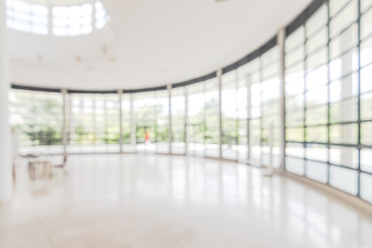Hotel or office building lobby blur background interior view toward reception hall, modern luxury white room space with blurry corridor and building glass wall window