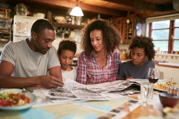 African American family planning late summer vacation together at cozy kitchen table, looking at maps and brochures, discussing travel route and destinations