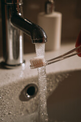 Maintaining oral hygiene by rinsing a toothbrush under hot water at the sink during a personal care routine