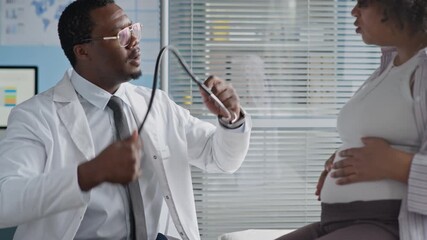 Medium hot of Black male healthcare professional examining pregnant woman using stethoscope in clinical setting, ensuring prenatal care and fetal health monitoring - Powered by Adobe