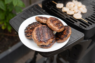 Grilled hamburgers on plate and shrimp on skewer at backyard barbecue