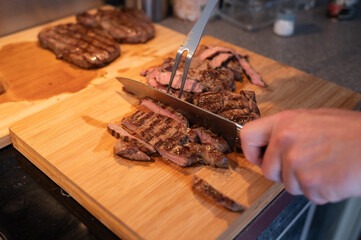 Grilled steak being sliced on wooden cutting board in kitchen setting