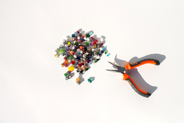 Colorful beads and pliers on white surface - crafting tools and materials