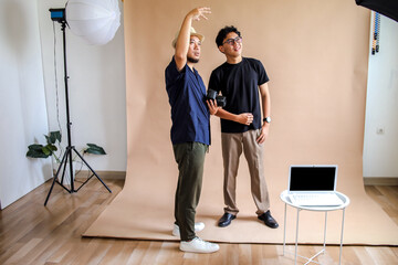 Asian Photographer Man Briefs Model In Front Of Seamless Beige Backdrop In Studio Setup