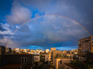 Rainbow arches over modern buildings in &Oslash;restad, Copenhagen, Denmark, blending urban architecture with dramatic summer skies.