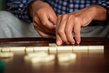 Close-up of adult son and elderly father's hands as they play dominoes together at home, highlighting connection, focus, and quiet bonding time.