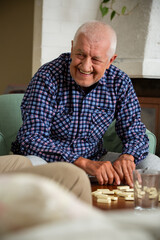 Elderly man shuffles domino tiles before a game. A warm family tradition captured in a timeless, quiet gesture of anticipation.