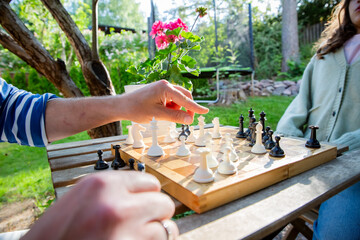 Close-up of a father and daughter playing chess in the garden. Summer family bonding through strategy and learning