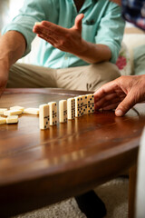 Close-up of adult son and elderly father's hands as they play dominoes together at home, highlighting connection, focus, and quiet bonding time.