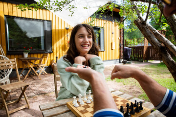 Father and tween daughter playing chess in their backyard on a summer day. Quality family time and mental development in a relaxed outdoor setting.