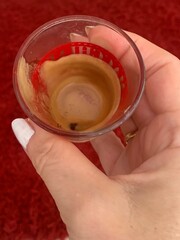 Woman holding an empty cup of espresso coffee against a red background 