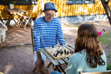 Father and tween daughter playing chess in their backyard on a summer day. Quality family time and mental development in a relaxed outdoor setting.