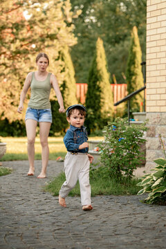 toddler boy running barefoot on path away from a woman.