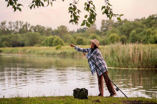 woman in a straw hat and plaid shirt fishing on  lake.