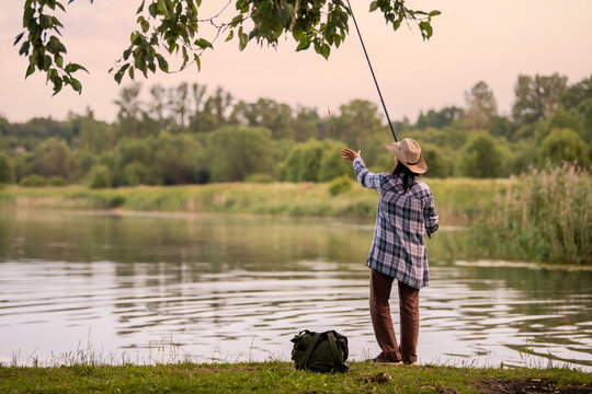 woman in a straw hat and plaid shirt fishing on bank  lake.