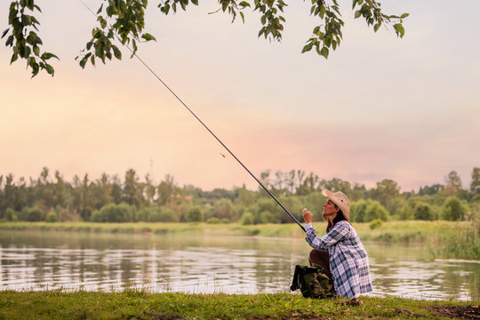 woman in a straw hat and plaid shirt fishing on  bank lake.