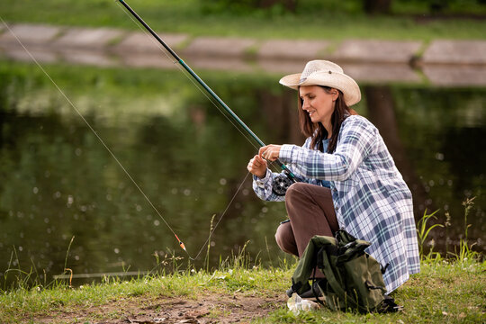 woman in a straw hat and plaid shirt fishing on  bank lake.
