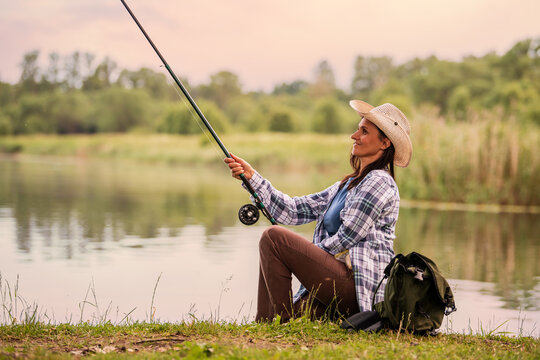 woman in a straw hat  fishing on the bank of a serene lake.