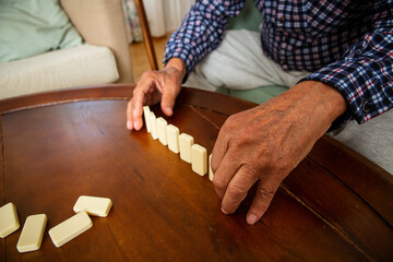 Close-up of elderly father's hands placing dominoes on the table during a quiet game with his adult son - a tender moment of age and connection.