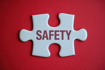 Fototapeta premium A White Puzzle Piece with the Word Safety Centered on a Red Background, Symbolizing Security and Protection in a Conceptual and Minimalist Design