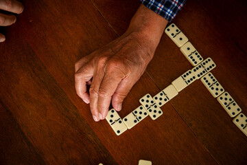 Close-up of adult son and elderly father's hands as they play dominoes together at home, highlighting connection, focus, and quiet bonding time.