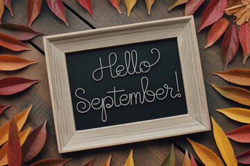 Autumnal Frame Displaying Hello September Message Surrounded by Colorful Fall Leaves on Rustic Wooden Surface for Seasonal Greetings