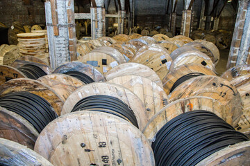 Many wooden reels with black electric cable stacked in a warehouse. Industrial stock. Electrical...