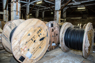 Large wooden spools with electrical cables stored in an old industrial warehouse. Industry and...