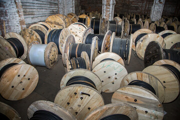 Many wooden reels with black electric cable coil for industrial wiring at old dusty warehouse...