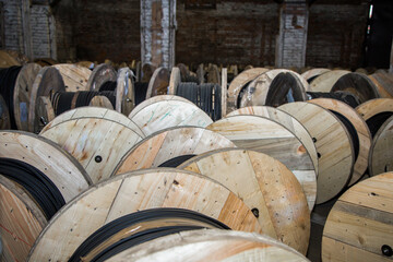Numerous large wooden spools with black electrical cable storage in warehouse. Industrial power...