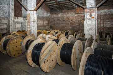 Rows of large wooden reels with black electric cable in an old and dusty industrial warehouse for...