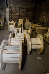 Several wooden cable spools in an industrial warehouse setting with brick walls. Empty reel for...