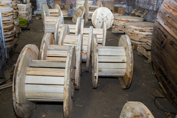 Wooden spools for cable storage lined up in a row inside an industrial warehouse or factory setting...