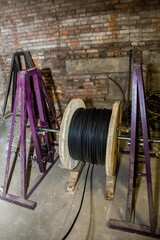 Black cable on a large wooden reel with purple metal supports, ready for pulling through a...