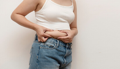 Close-up of a woman in jeans and tank top pinching side belly fat, highlighting natural body shape...