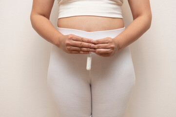 Close-up of woman in white outfit holding a tampon, representing feminine hygiene, period care, and...