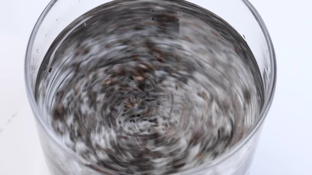 chia seeds being stirred in a glass of water with a spoon forming swirling motion top view