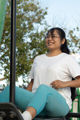Young woman exercising on outdoor gym equipment smiling and looking away