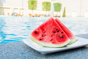 Watermelon slices on a white plate near the outdoor pool. Vacation, summer concept.