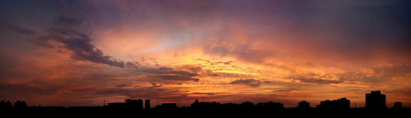 The dying sunset after sunset over the black silhouette of the city. The farewell fire heavenly sun before night. Fabulous glow of orange, purple violet halftones. Wide banner for a website or screen