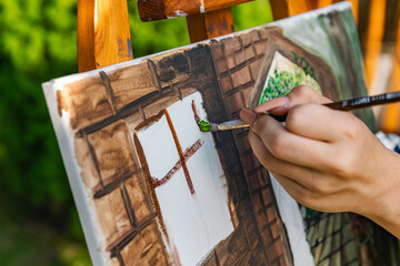 Close-up of someone skillfully painting on a canvas. The artwork looks like it depicts a rustic...