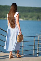 Woman with brown long hair in summer dress walking near a lake