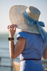 Woman with brown long hair and straw hat in summer dress walking near a lake