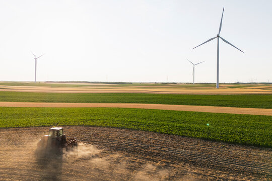 Aerial view of tractor working in field with wind turbines for renewable energy