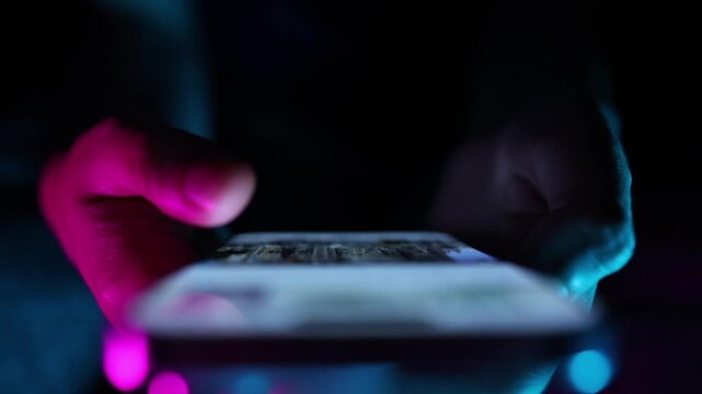 Woman watching and reading online news on smartphone, scrolling up and down looking in phone screen in dark room.