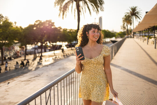 Smiling fashionable woman exploring sunny city with shopping bag