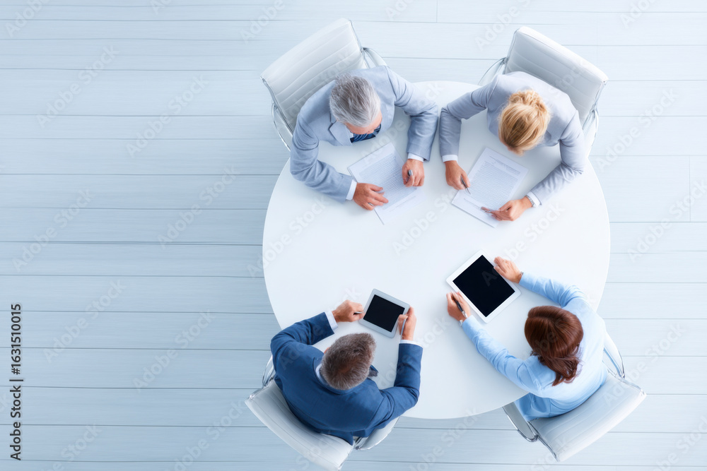 Poster aerial view of a business meeting with four professionals discussing over tablets and documents on a